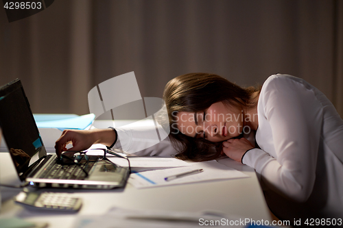 Image of tired woman sleeping on office table at night