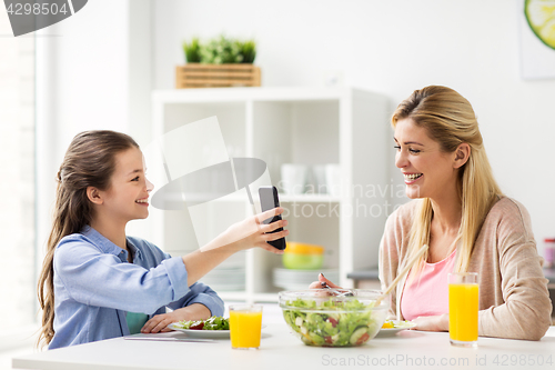Image of happy family with smartphone having dinner at home