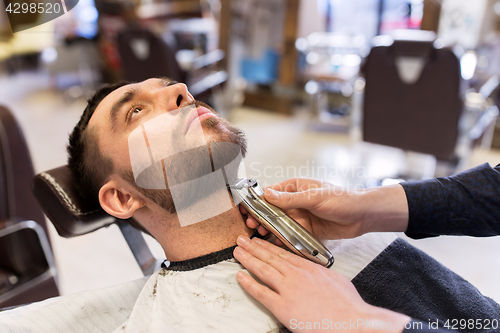 Image of man and barber with trimmer cutting beard at salon