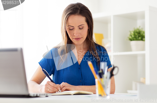 Image of happy woman writing to notebook at office