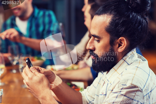Image of man with smartphone and friends at restaurant