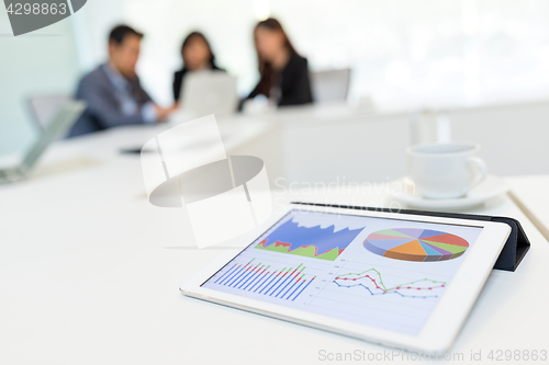 Image of Digital tablet showing graph with business partners discussing i