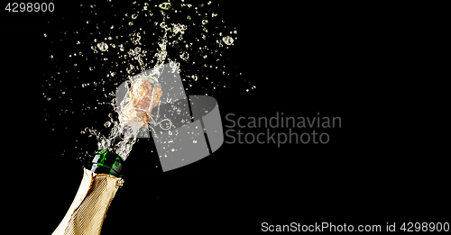 Image of Champagne cork popping and splashing on black background