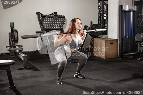 Image of Attractive fit woman works out with dumbbells as a fitness conceptual over gray gym background.