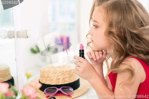 Image of A little girl with cosmetics. She is in mother\'s bedroom, sitting near the mirror.