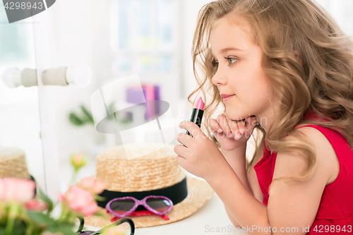 Image of A little girl with cosmetics. She is in mother\'s bedroom, sitting near the mirror.