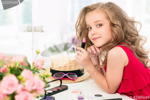 Image of A little girl with cosmetics. She is in mother\'s bedroom, sitting near the mirror.