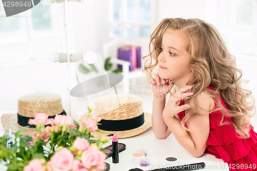 Image of A little girl with cosmetics. She is in mother\'s bedroom, sitting near the mirror.