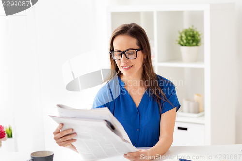 Image of happy woman in glasses reading newspaper at office