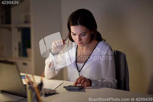 Image of woman with calculator and papers at night office