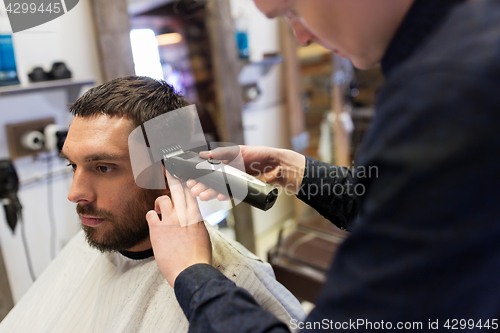 Image of man and barber with trimmer cutting hair at salon