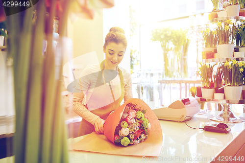 Image of smiling florist woman packing bunch at flower shop