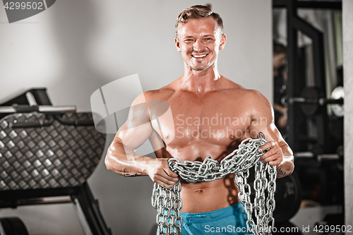Image of Attractive hunky black male bodybuilder doing bodybuilding pose in gym with iron chains