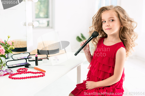 Image of A little girl with cosmetics. She is in mother\'s bedroom, sitting near the mirror.