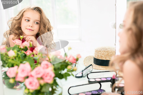 Image of A little girl with cosmetics. She is in mother\'s bedroom, sitting near the mirror.