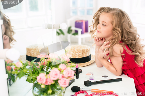 Image of A little girl with cosmetics. She is in mother\'s bedroom, sitting near the mirror.