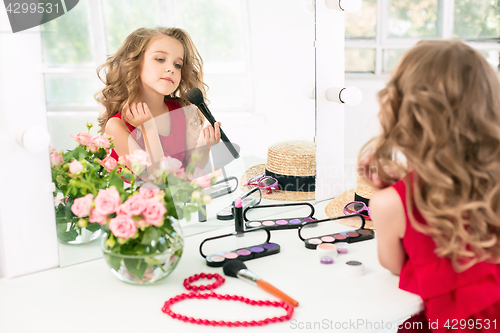 Image of A little girl with cosmetics. She is in mother\'s bedroom, sitting near the mirror.