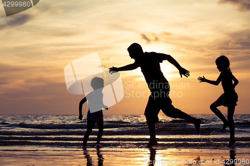 Image of Father and children playing on the beach at the sunset time.