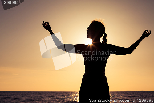 Image of woman open arms under the sunset at sea.