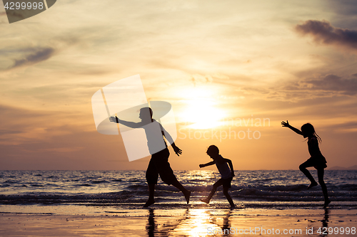 Image of Father and children playing on the beach at the sunset time.