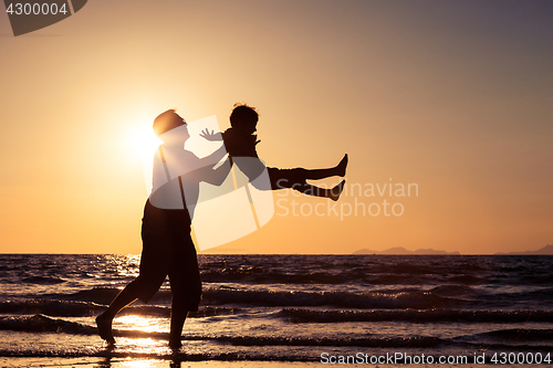 Image of Father and son playing on the beach at the sunset time.