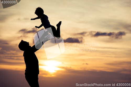 Image of Father and son playing on the beach at the sunset time.