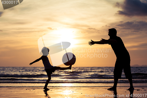Image of Father and son with ball playing soccer on the beach at the day 