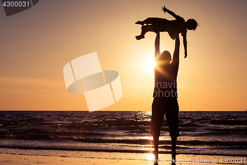 Image of Father and son playing on the beach at the sunset time.