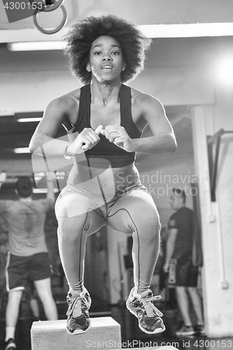 Image of black female athlete is performing box jumps at gym