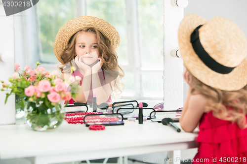 Image of A little girl with cosmetics. She is in mother\'s bedroom, sitting near the mirror.