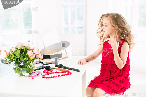 Image of A little girl with cosmetics. She is in mother\'s bedroom, sitting near the mirror.