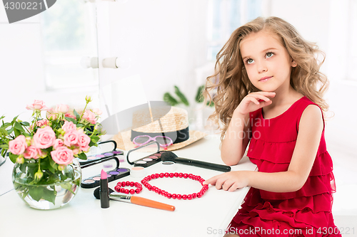 Image of A little girl with cosmetics. She is in mother\'s bedroom, sitting near the mirror.