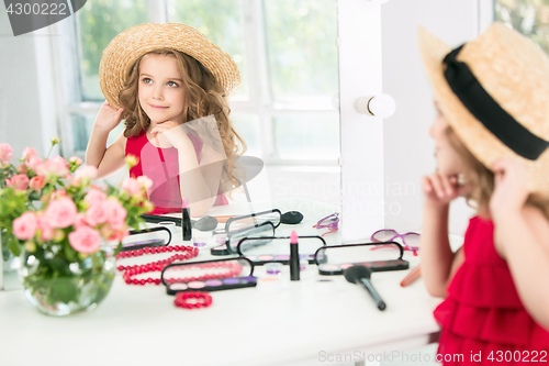 Image of A little girl with cosmetics. She is in mother\'s bedroom, sitting near the mirror.