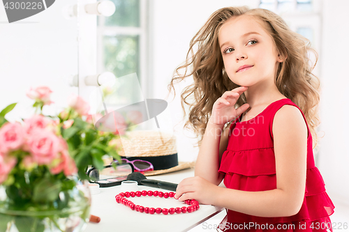 Image of A little girl with cosmetics. She is in mother\'s bedroom, sitting near the mirror.