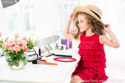 Image of A little girl with cosmetics. She is in mother\'s bedroom, sitting near the mirror.