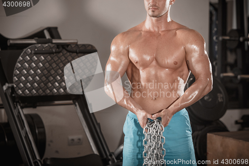 Image of Attractive hunky black male bodybuilder doing bodybuilding pose in gym with iron chains