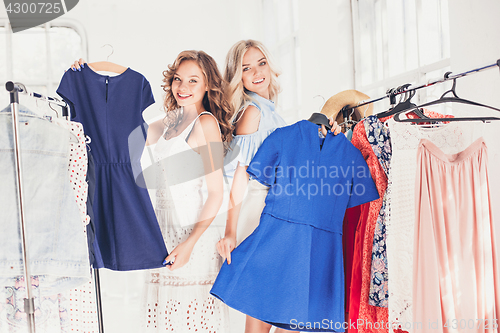 Image of The two young pretty girls looking at dresses and try on it while choosing at shop