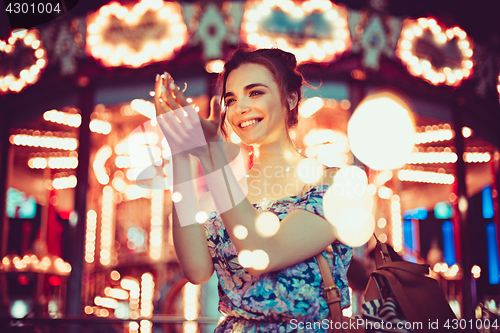 Image of Beautiful young woman smiling and talking garlands of lights at city