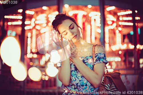 Image of Beautiful young woman smiling and talking garlands of lights at city