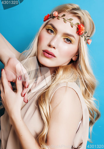 Image of young pretty blond girl with curly blond hair and little lowers happy smiling on blue sky background, lifestyle people concept 