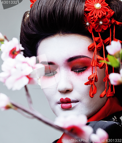 Image of young pretty geisha in black kimono among sakura, asian ethno close up