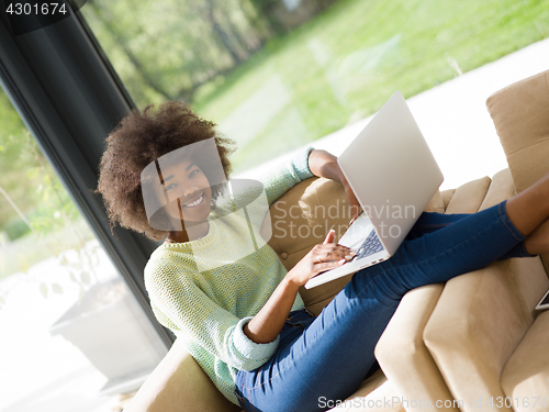 Image of African American woman using laptop on sofa