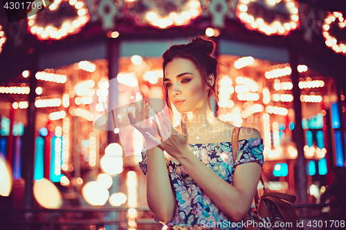 Image of Beautiful young woman smiling and talking garlands of lights at city