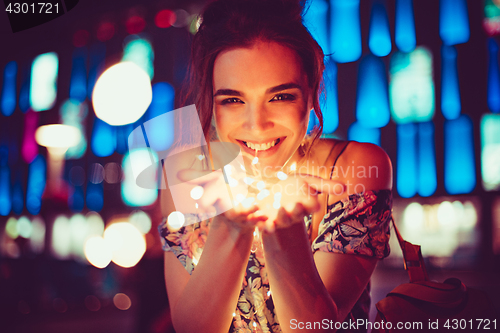 Image of Beautiful young woman smiling and talking garlands of lights at city