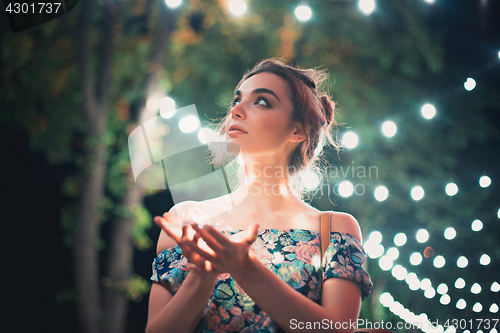 Image of Beautiful young woman smiling and talking garlands of lights at city