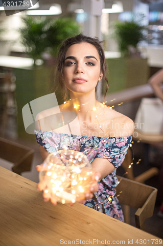 Image of Beautiful young woman smiling and talking garlands of lights at city