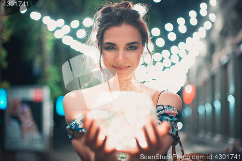 Image of Beautiful young woman smiling and talking garlands of lights at city