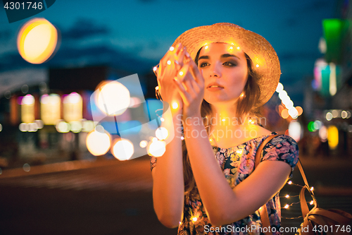 Image of Beautiful young woman smiling and talking garlands of lights at city