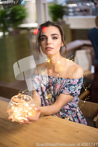 Image of Beautiful young woman smiling and talking garlands of lights at city