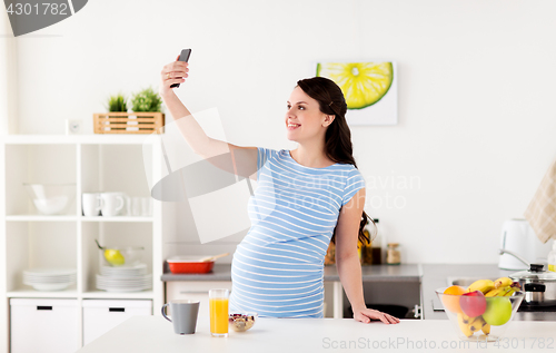 Image of happy pregnant woman with smartphone at kitchen